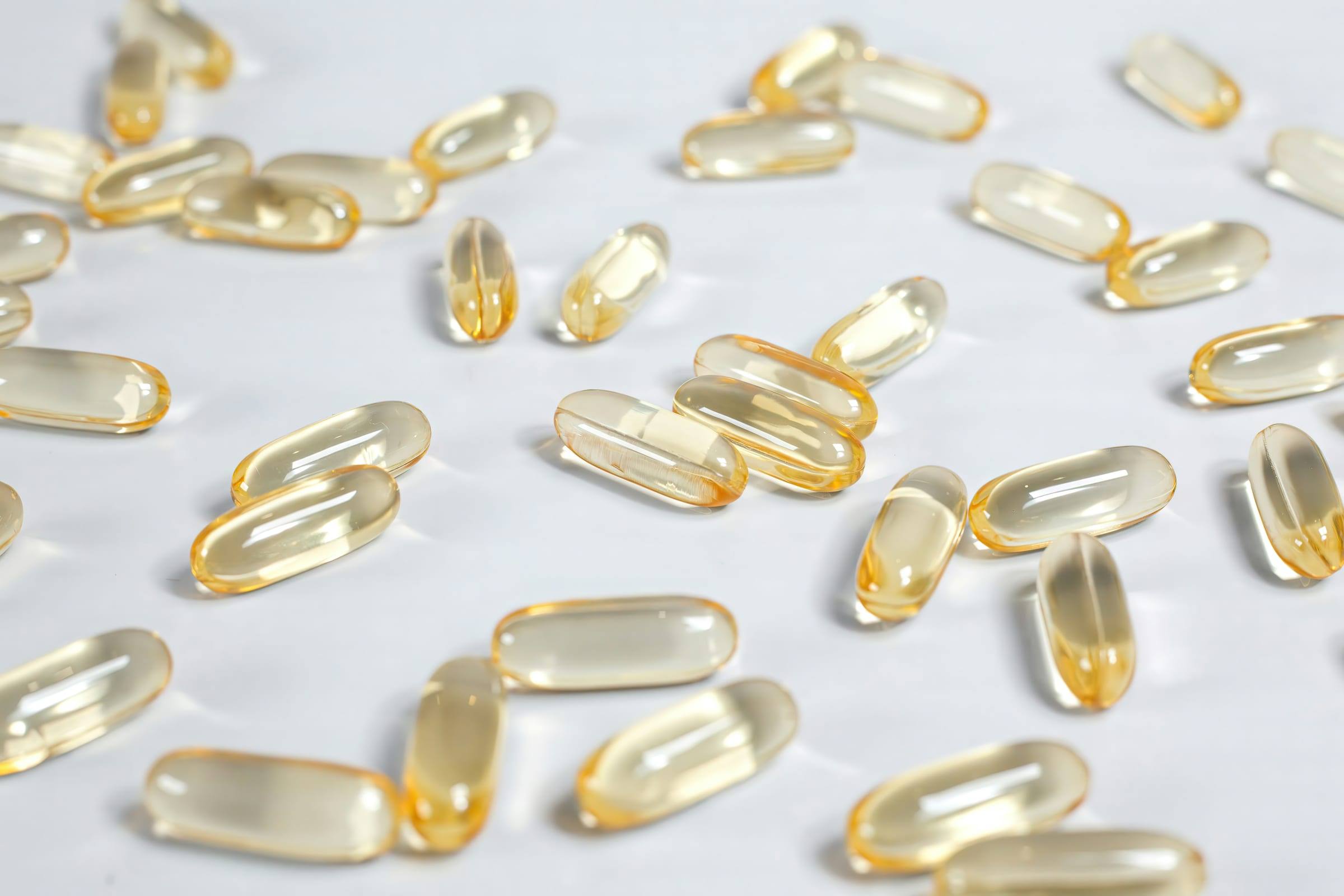 Clear amber softgel capsules scattered on a white surface.